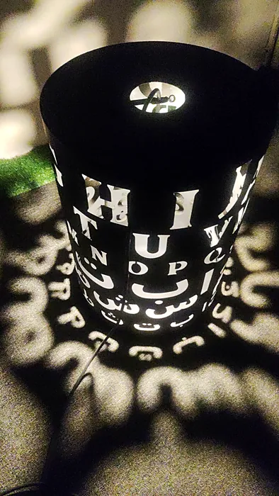 Laser-cut Arabic and English letter lantern casting light patterns
